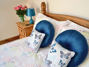 A bed with blue pillows, a wooden headboard, a bedside table with a lamp, and a vase with flowers. - 2 bedroom accommodation in Hartland, near Bideford (Hartland, near Bideford)