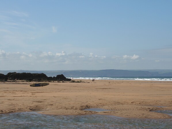 A beach with a clear sky, rocky outcrops, and a calm sea.