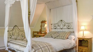 A four-poster canopy bed with a wooden headboard, a bedside table with a lamp, and a mirror on the wall.