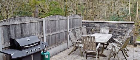 Une terrasse extérieure avec un barbecue, des chaises et une table.