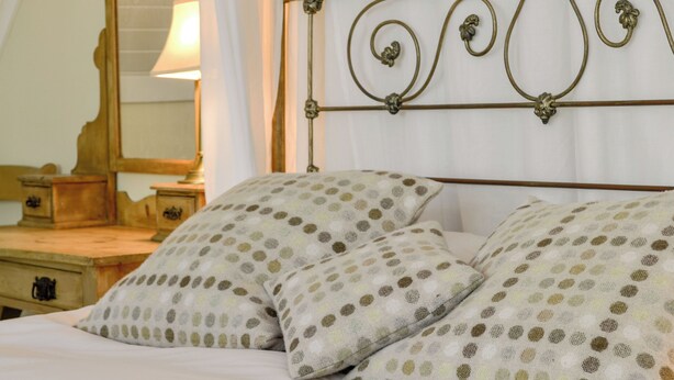 A bed with two pillows featuring a polka dot pattern, a wooden nightstand with a lamp, and a mirror on the wall.