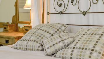 A bed with two pillows featuring a polka dot pattern, a wooden nightstand with a lamp, and a mirror on the wall.