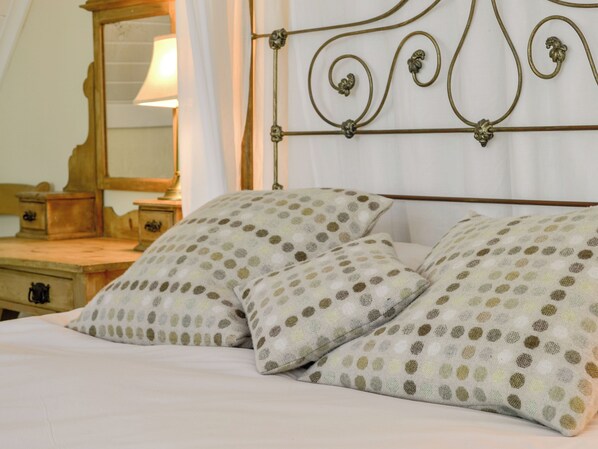 A bed with two pillows featuring a polka dot pattern, a wooden nightstand with a lamp, and a mirror on the wall.