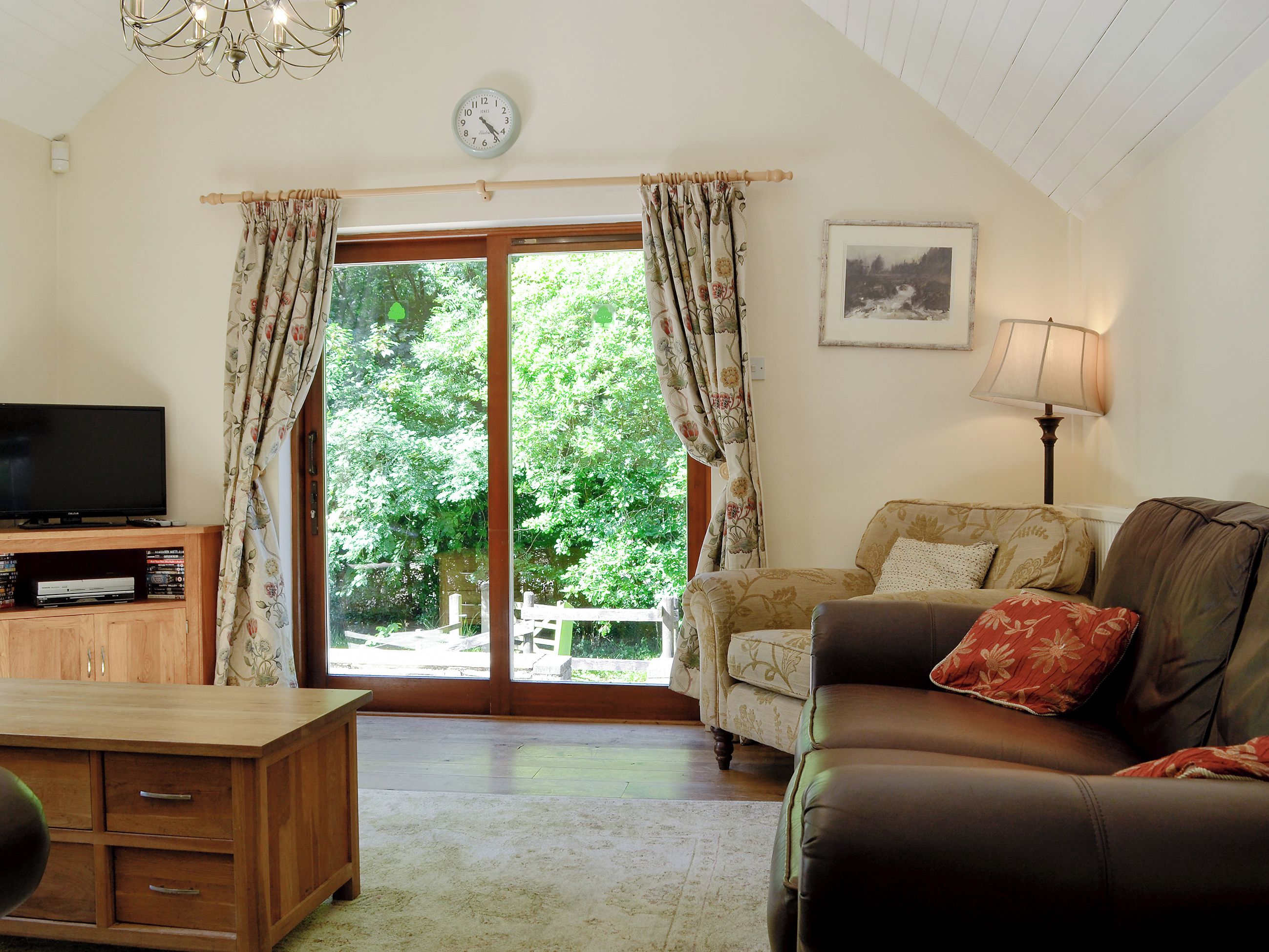 A living room with a television, a sofa, a lamp, and a large window with curtains.