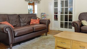 A brown leather sofa with floral cushions, a wooden coffee table, and a glass door leading to a room with a white interior.