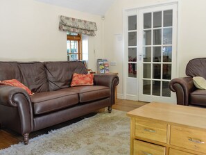 A brown leather sofa with floral cushions, a wooden coffee table, and a glass door leading to a room with a white interior.