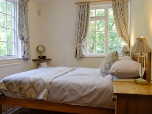 A neatly made bed with a patterned blanket, a bedside lamp, and a small shelf with a mirror and towels.