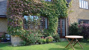 Une maison en pierre aux murs recouverts de lierre, avec une pelouse et une table en bois.