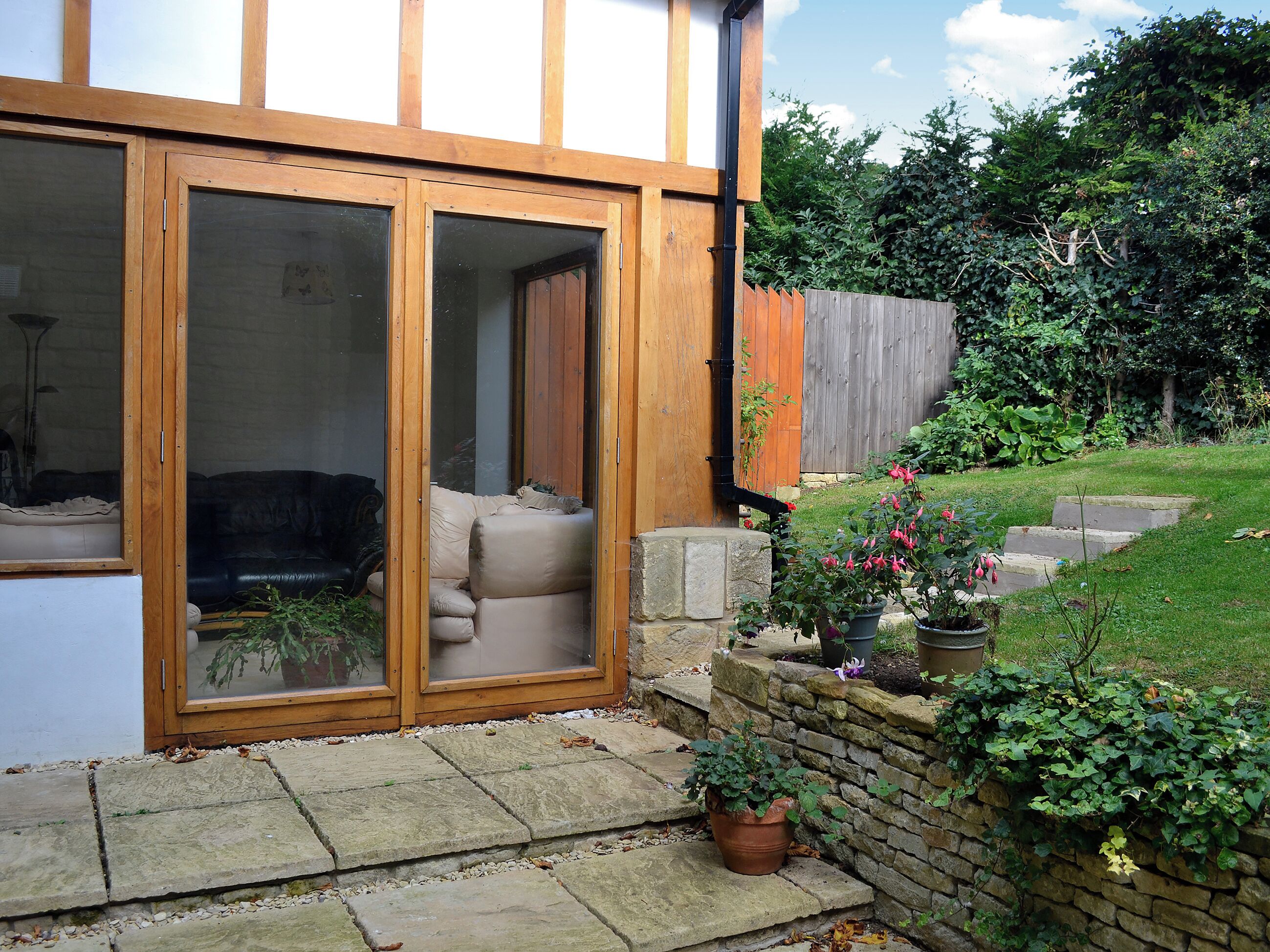 A residential property with a sliding glass door entrance, a stone pathway, a stone wall, and a garden with potted plants.