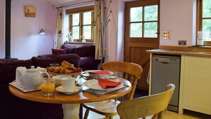 A cozy living room with a sofa, a dining table set for breakfast, and a kitchen area with a dishwasher. - 1 bedroom accommodation in Swerford, near Chipping Norton (Swerford, near Chipping Norton)
