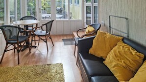 A cozy living room with a black leather sofa, yellow cushions, wicker chairs, and a small round table. - 4 bedroom accommodation in East Runton, near Cromer (East Runton, near Cromer)