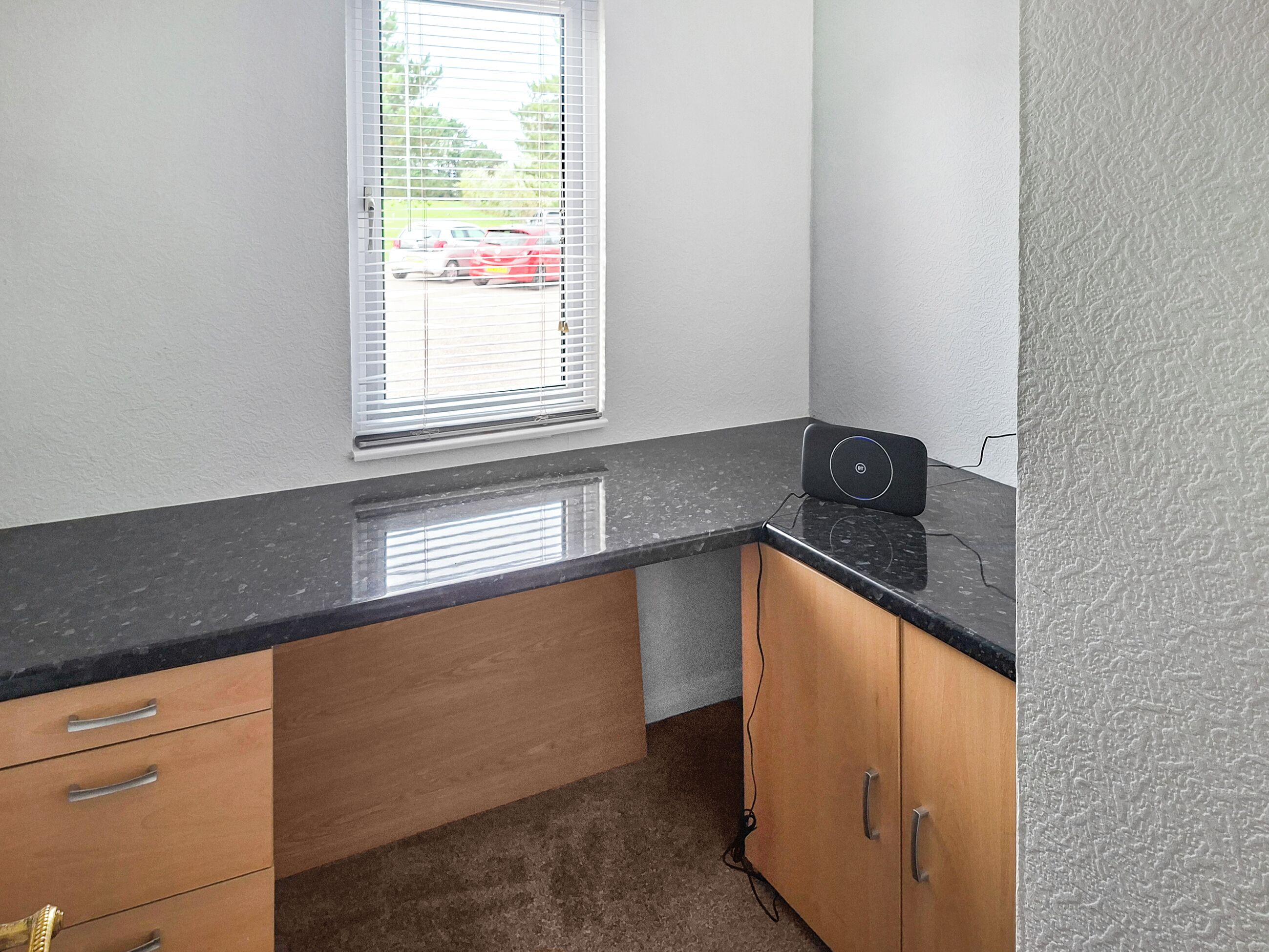 Eine Küche mit schwarzer Arbeitsplatte, Holzschränken und einem Fenster mit Jalousien.