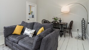 Un salon moderne avec un canapé gris, des coussins jaunes, une table à manger avec des chaises et un lampadaire.