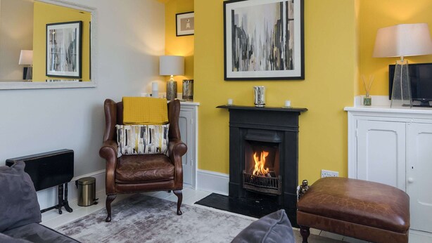 Un salon avec une cheminée, un fauteuil en cuir marron, un canapé et un mur d’accent jaune.