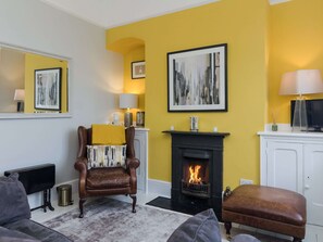 A living room with a fireplace, a brown leather armchair, a sofa, and a yellow accent wall. - 3 bedroom accommodation in Ramsgate (Ramsgate)
