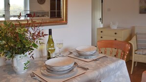 A dining table set with plates, a wine bottle, and glasses, a vase with greenery, and a mirror above the table. - Maplehurst Barn Stables (Staplehurst, near Maidstone)