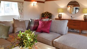 A cozy living room with a sofa, cushions, a side table with lamps, a mirror, and a window with curtains. - Maplehurst Barn Stables (Staplehurst, near Maidstone)