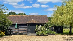 A rustic building with a sloped roof, surrounded by greenery and a gravel driveway. - Maplehurst Barn Stables (Staplehurst, near Maidstone)