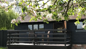 A wooden deck with benches, a brick wall, and a house with windows in the background. - Maplehurst Barn Stables (Staplehurst, near Maidstone)
