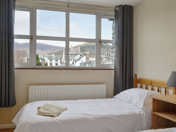 A hotel room with a bed, a window with a view of buildings and hills, a radiator, and a wooden headboard.