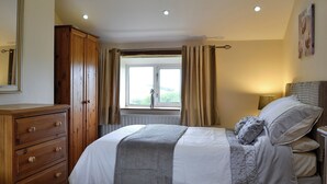 A bedroom with a bed, a wooden dresser, a window with curtains, and a view of greenery outside. - Lakes, mountains or beaches - how about the best of all three. (Bigrigg, near Egremont)