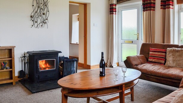 A cozy living room with a wood-burning stove, a leather sofa, a wooden coffee table, and a decorative wall piece. - Lakes, mountains or beaches - how about the best of all three. (Bigrigg, near Egremont)