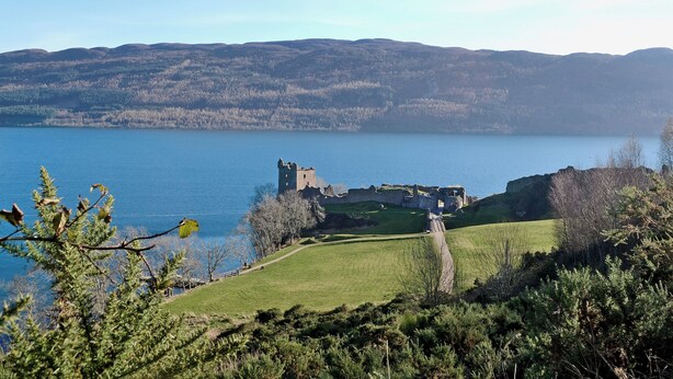 A historic castle ruin by a lake with a clear view of the surrounding hills.