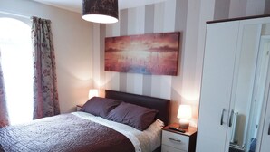 Une chambre d’hôtel avec un lit, des lampes de chevet, un tableau au mur, une armoire et une fenêtre avec des rideaux.