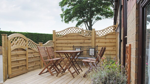 Une terrasse en bois avec une table et des chaises, une clôture en bois et un pot de fleurs.
