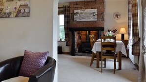 A cozy living room with a fireplace, a dining table set for two, and a comfortable armchair. - 2 bedroom accommodation in Bigrigg, near Egremont (Bigrigg, near Egremont)
