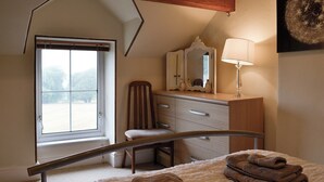 A bedroom with a wooden ceiling, a large window, a chair, a dresser, a mirror, a lamp, and a bed with towels. - 2 bedroom accommodation in Bigrigg, near Egremont (Bigrigg, near Egremont)