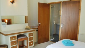 A hotel room with a wooden desk, a mirror, a shower, and two beds with towels. - 1 bedroom accommodation in Mevagissey, near St Austell (Mevagissey, near St Austell)