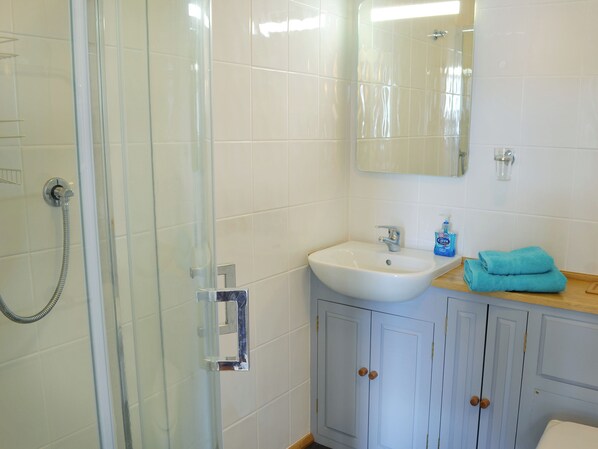 Une salle de bain avec une douche à parois de verre, un lavabo blanc, un miroir et un meuble-lavabo en bois.