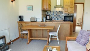 A cozy kitchen with wooden cabinets, a dining table, and a sofa. - 1 bedroom accommodation in Mevagissey, near St Austell (Mevagissey, near St Austell)