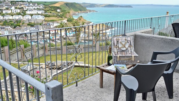 A balcony with a view of the sea, a wicker picnic basket, a bottle of champagne, and a table with magazines. - 1 bedroom accommodation in Mevagissey, near St Austell (Mevagissey, near St Austell)