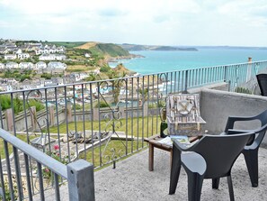 Un balcon avec vue sur la mer, un panier de pique-nique en osier, une bouteille de champagne et une table avec des magazines.