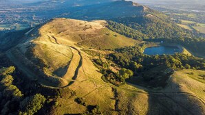 An aerial view of a hilly landscape with a winding road, a lake, and a distant mountain range. - 0 bedroom accommodation in Upper Welland, Malvern (Upper Welland, Malvern)