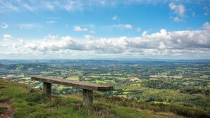 A stone bench overlooking a vast landscape with rolling hills and fields under a partly cloudy sky. - 0 bedroom accommodation in Upper Welland, Malvern (Upper Welland, Malvern)