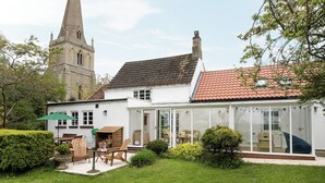 A traditional white building with a red-tiled roof, a large windowed extension, and a garden with a lawn and a wooden table and chairs. - 3 bedroom accommodation in Denford, near Thrapston (Denford, near Thrapston)