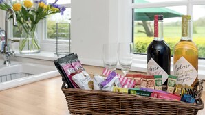 A wicker basket filled with various snacks, a bottle of Belvoir Chardonnay, and two glasses on a kitchen counter near a window with a view of greenery. - 3 bedroom accommodation in Denford, near Thrapston (Denford, near Thrapston)