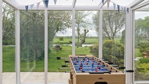 A foosball table in a glass-enclosed room with a view of a grassy field and trees. - 3 bedroom accommodation in Denford, near Thrapston (Denford, near Thrapston)