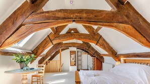 A bedroom with a sloped ceiling, wooden beams, a bed, a table with a vase of flowers, and a chair. - 4 bedroom accommodation in Stratton, near Bude (Stratton, near Bude)