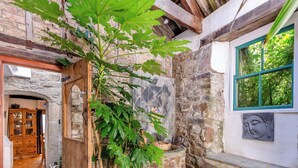 A rustic stone building with a wooden door, a window with a Buddha sculpture, and a large leafy plant growing outside. - 4 bedroom accommodation in Stratton, near Bude (Stratton, near Bude)