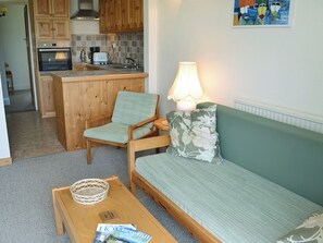 A compact living space with a kitchenette, a sofa, a chair, a lamp, and a magazine on a coffee table.
