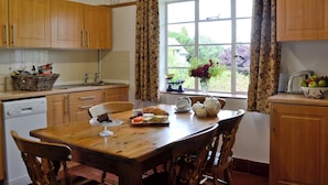 Cozinha com armários de madeira, uma mesa de jantar com cadeiras, uma janela com cortinas e vista para o verde lá fora.