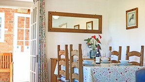 Ein Essbereich mit einem Tisch für vier Personen, Holzstühlen, einem Spiegel an der Wand und einer Tür, die nach draußen führt.