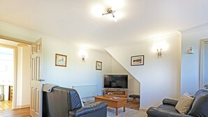 Ein Wohnzimmer mit einer Couch, einem Couchtisch, einem Fernseher und einer Treppe.