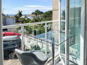 Un balcon doté d’une table et de chaises en verre, offrant une vue sur une zone côtière avec des bâtiments et un château.