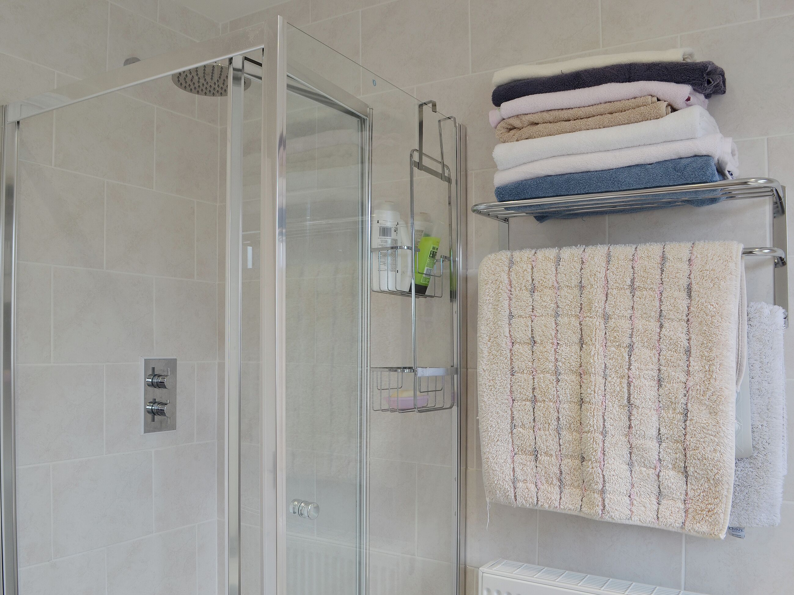 Un bagno moderno con doccia vetro, porta asciugamani con asciugamani piegati e pensile con articoli da toilette.
