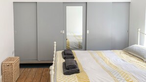 Ein Schlafzimmer mit einem Bett, einem grauen Kleiderschrank und einem kleinen Korbwäschekorb.